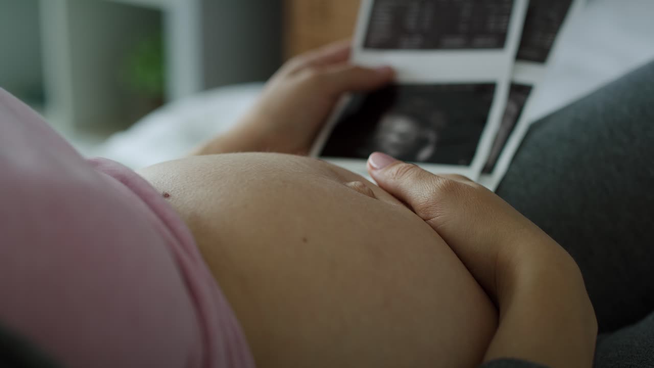 Video di una donna incinta che si accarezza l'addome e sfoglia immagini ecografiche