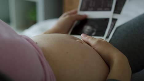 video de una mujer embarazada acariciando el abdomen y mirando imágenes de ultrasonido.