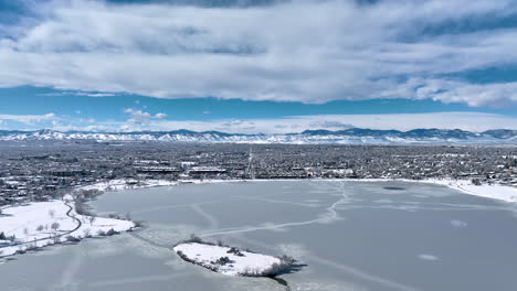 aerial drone moving backwards to reveal frozen sloan lake, denver during winter storm showing rocky mountains in background