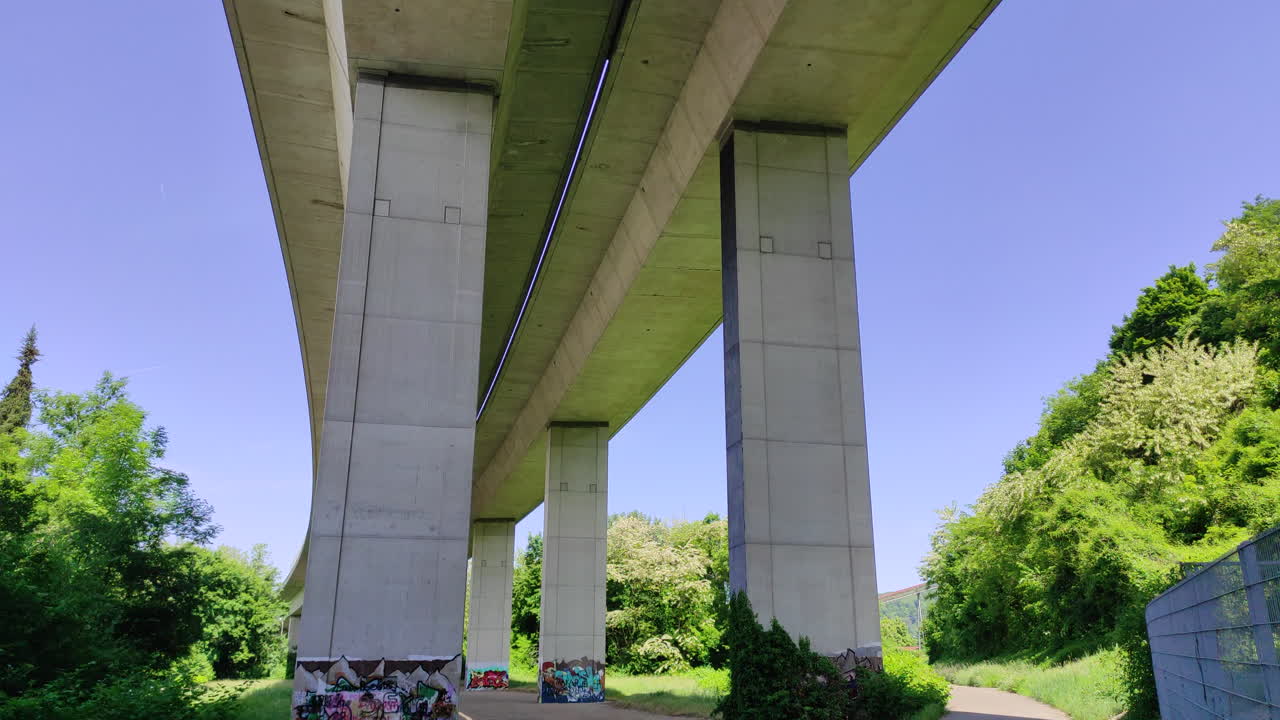 Underneath a highway with pillars, trees, bike path, tilt-up shot
