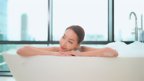 asian woman relaxing on resort-style bathtub, modern skyline on background