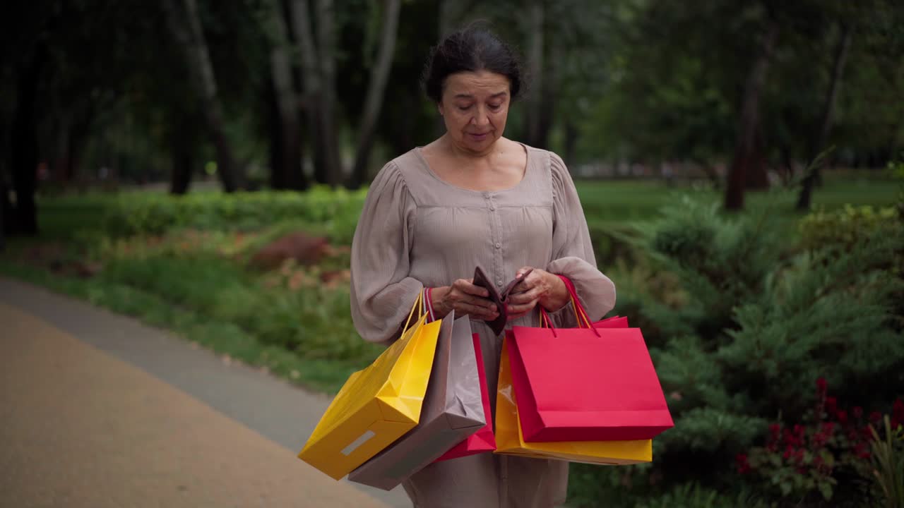 한 표정으로 카메라를 바라보는 빈 지갑을 열고 쇼핑백을 들고 있는 당황한 백인 시니어 쇼핑객.