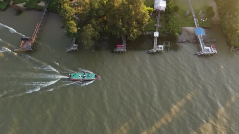 Collective-bus-boat-sailing-close-to-private-docks-of-Parana-river-delta-at-sunset,-Argentina