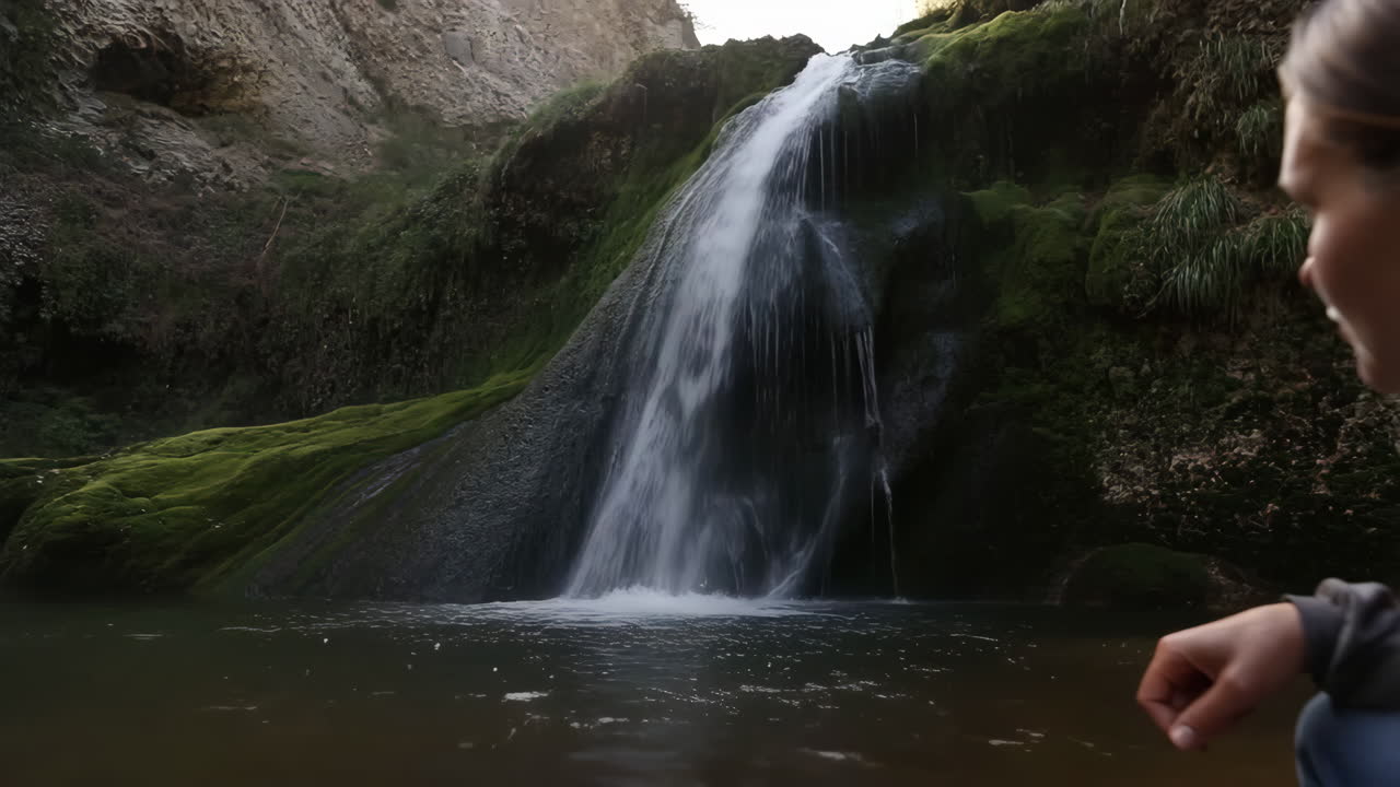 Una persona che osserva una bellissima cascata che si getta in una pozza naturale tra rocce coperte di muschio
