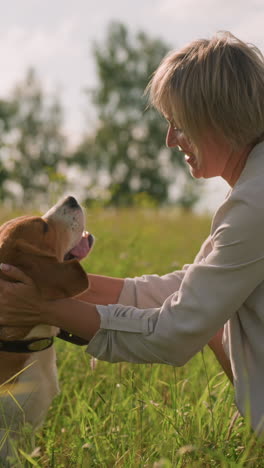 el dueño del perro en cuclillas en un campo cubierto de hierba frota cariñosamente la cabeza del perro mientras el perro lamia su boca felizmente en un día soleado y brillante, rodeado de exuberante vegetación y naturaleza