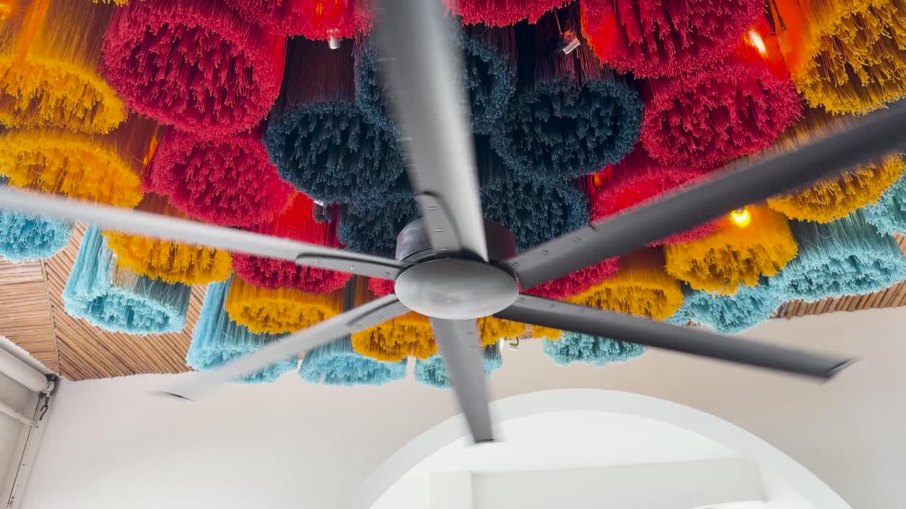 un ventilador de techo gira debajo de decoraciones vibrantes y texturizadas en un restaurante bien iluminado, creando un efecto visual dinámico