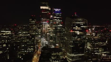 Elevated-view-of-group-of-modern-tall-buildings-in-City-financial-and-economic-centre-at-night.-Forwards-fly-towards-skyscrapers.-London,-UK