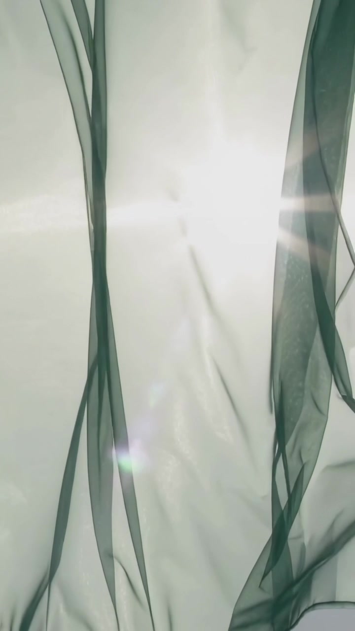 Vertical video: Sun rising at window, sheer curtain with dark ribbons rippling by draft, sun flare