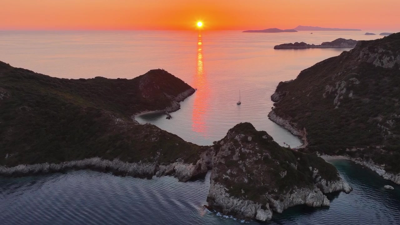 Vista aerea al tramonto della baia di Porto Timoni a Corfù, Grecia, con barca a vela e cielo arancione sul mare