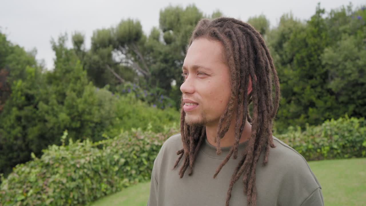 Un uomo afroamericano sui 20 anni si gira e sorride nel cortile, mentre la telecamera zooma vicino a un'altalena, indossando una maglia color oliva.