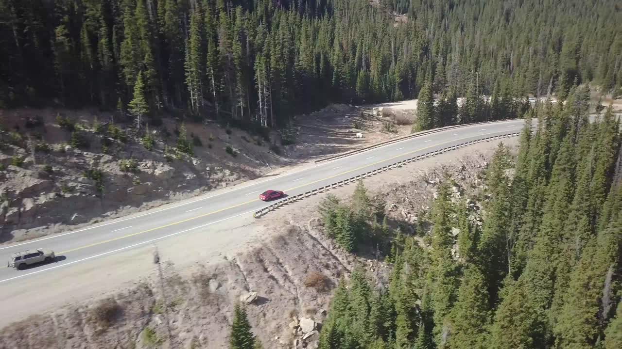 Trucking panning shot following a red car through pine trees on a mountain in the mid-west