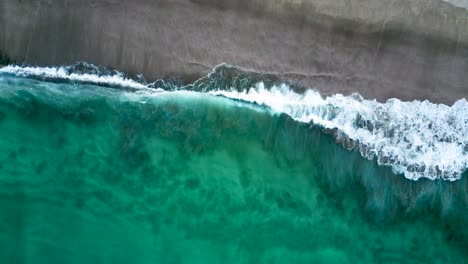 Crystal-clear-water-waves-crash-on-Piha-Beach's-blackish-sand-in-New-Zealand