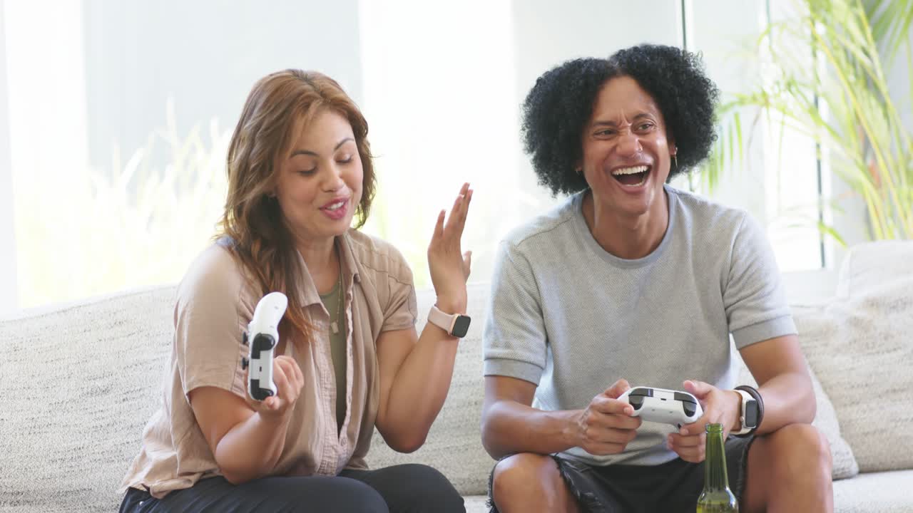 African American couple celebrating after scoring while holding white controllers on sofa at home