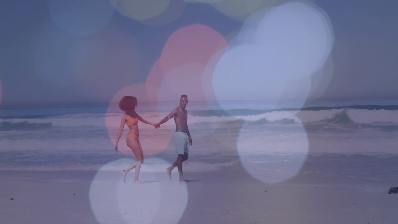 Coppia che entra da sinistra, tenendosi per mano, camminando lungo la riva per un video lifestyle, con una sovrapposizione bokeh in movimento.