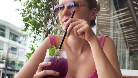 mujer disfrutando de una bebida púrpura en un patio de café