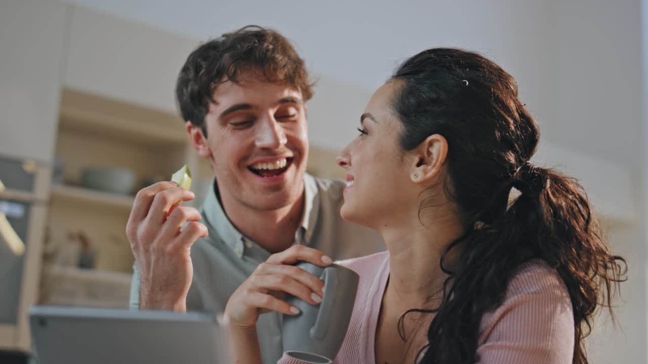una pareja desayunando llamando en línea usando una tableta moderna en la cocina de cerca.