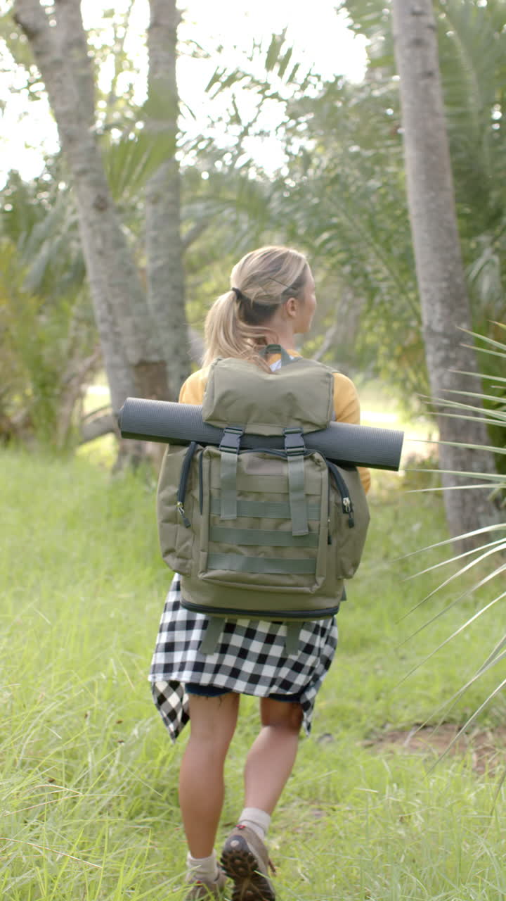 Vertical video: Hiking in forest, woman with backpack and yoga mat exploring nature trail