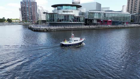 aerial drone flight over salford quays at media city and manchester ship canal following a small fishing boat as it travels along the water