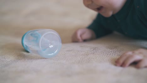 funny baby plays with bottle resting on large soft bed