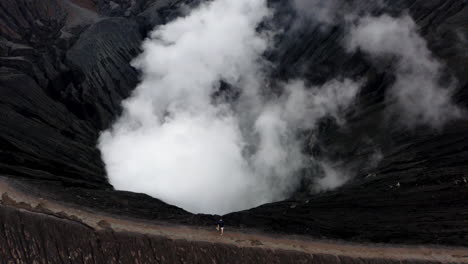 man stands on rim of mt. bromo, east java. aerial shot reveals rugged indonesia