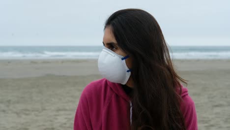 retrato de perfil de una morena casual con mascarilla médica protectora en la playa, fondo oceánico, relajada, pensativa