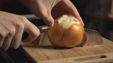 slicing a whole white onion using a knife on wooden chopping board