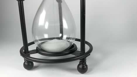 the bottom part of an hourglass with black metallic base filling up with white sands of time, isolated, still, timelapse