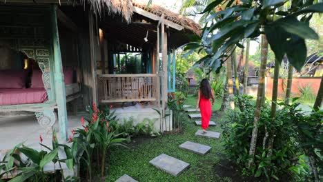 young asian in red dress walking on footpath through tropical garden at traditional bali villa