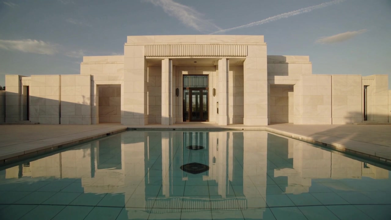 Responding to ripples, stone building and reflecting pool shimmering on paved terrace with drains