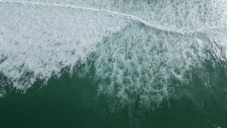 long aerial top down of powerful ocean waves crashing at the beach