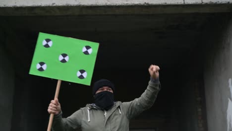 a man wearing a black mask on his face holds a poster in his hands walks straight and waves to them. copy space tracking points. blank green screen board.