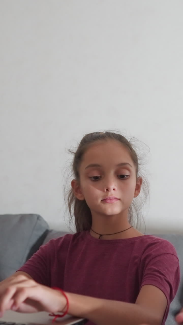 Una niña pequeña está escribiendo en un portátil en el salón y su hermano la distrae mostrándole con orgullo un trabajo escrito. Ella lo mira con interés y, a continuación, le levanta el pulgar en señal de apoyo.