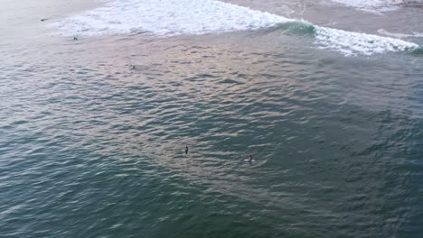 Antenne:-Surfer-Sitzen-Auf-Surfbrettern-Hinter-Brechenden-Wellen,-Blick-Auf-Den-Sonnenuntergang