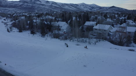 Drone-view-flying-over-people-walking-back-home-through-thick-layers-of-snow-by-the-side-of-the-road-around-Park-City-in-Utah-during-winter-at-sunset