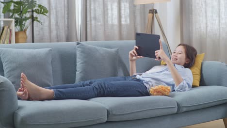 teenager relaxing on sofa with tablet and snacks