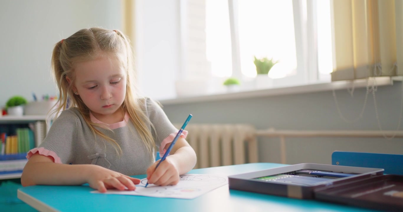 Geconcentreerd klein meisje tekent met een potlood aan een blauw bureau