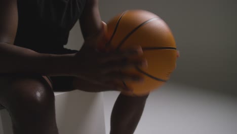 close up studio shot of seated male basketball player with hands holding ball 5