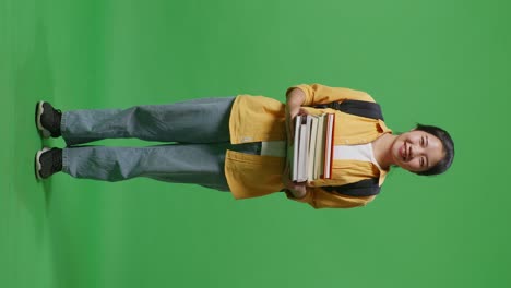 full body of asian woman student with a backpack holding some books and smiling to camera while standing in the green screen background studio