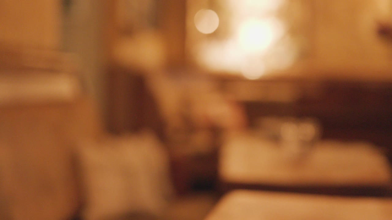 Two dark stout beers on a wooden pub table are picked up, leaving a softly lit, warmly blurred background with inviting, ambient lighting and shallow focus