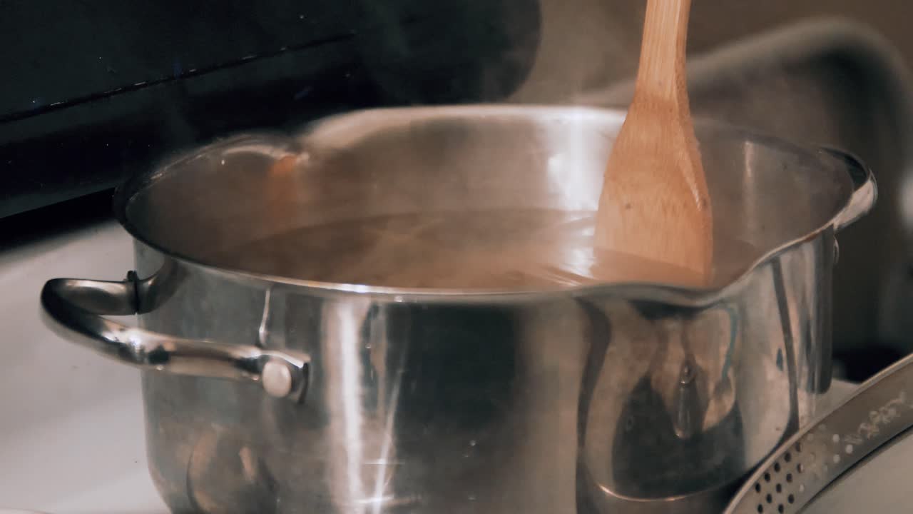 Content Caucasian male chef stirs spaghetti pasta in boiling hot water on kitchen stove, slow motion