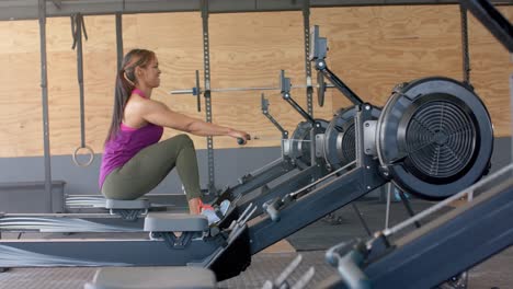 Determined-unaltered-biracial-woman-exercising-on-rowing-machine-at-gym,-in-slow-motion