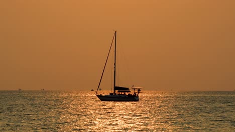 scenic silhouette of a yacht with orange and pinkish skies on the horizon with calm waters in bangsaray near pattaya, thailand