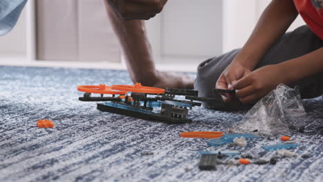 close up of grandfather with grandson sitting on rug at home building model helicopter together