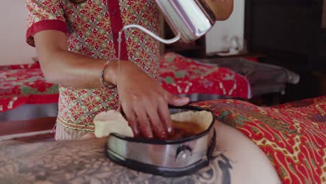 close up of a spa therapist pouring oil into a wax-lined container on the back on a patient enjoying a kati vasti treatment