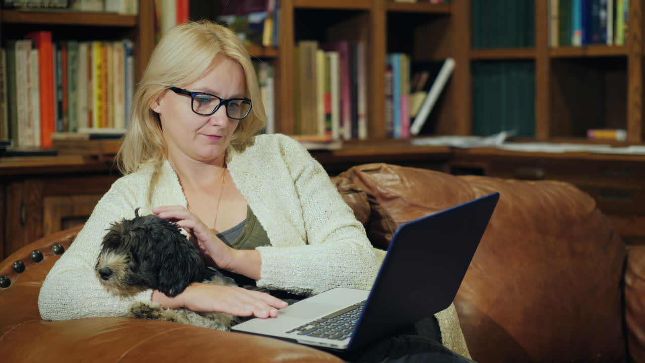 한 여성이 고급스러운 홈 라이브러리에서 작은 개를 안고 휴식을 취하고 있습니다.