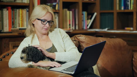 a woman relaxes in a luxurious home library holds a small dog