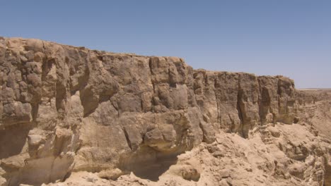 aerial of bare rocky cliff face in middle east desert on sunny day. mitzpe ramon, israel.