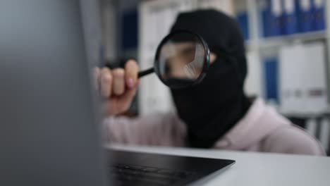 internet stealing masked person looks at computer screen with magnifying glass