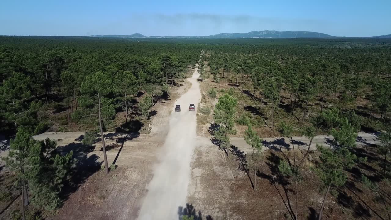 dos coches clásicos corren por un camino de tierra vacío con una vista épica