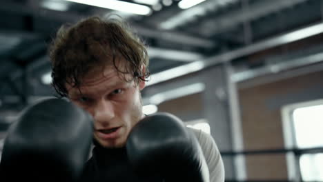 stressed sportsman showing strength on ring. kickboxer throwing blows at gym